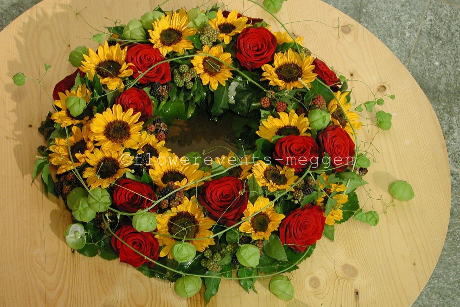Urnenkranz aus kleinen Sonnenblumen und roten Rosen